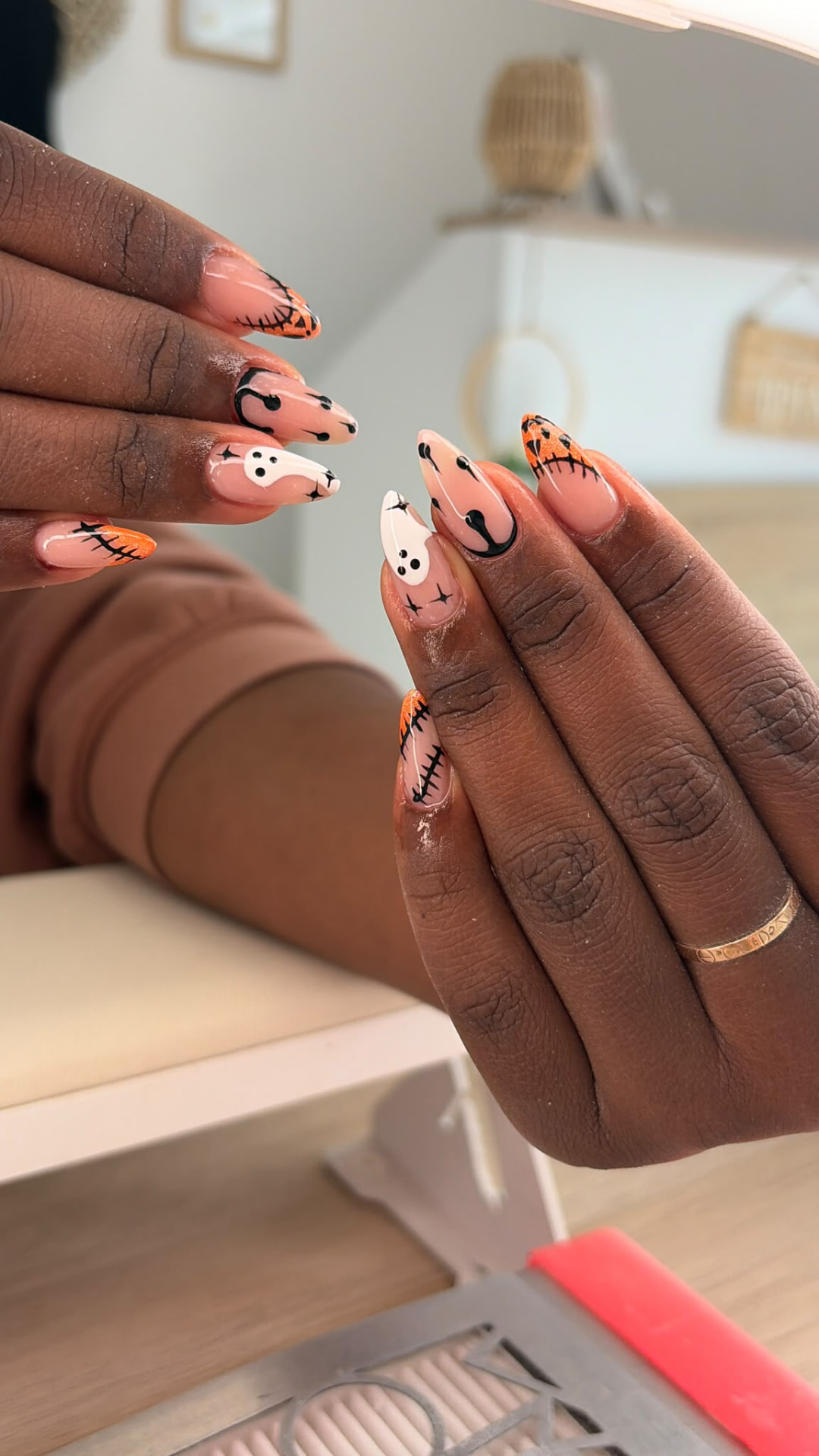 Nail art sur ongles amande, base nude, fantômes blancs et pointes orange pailletées